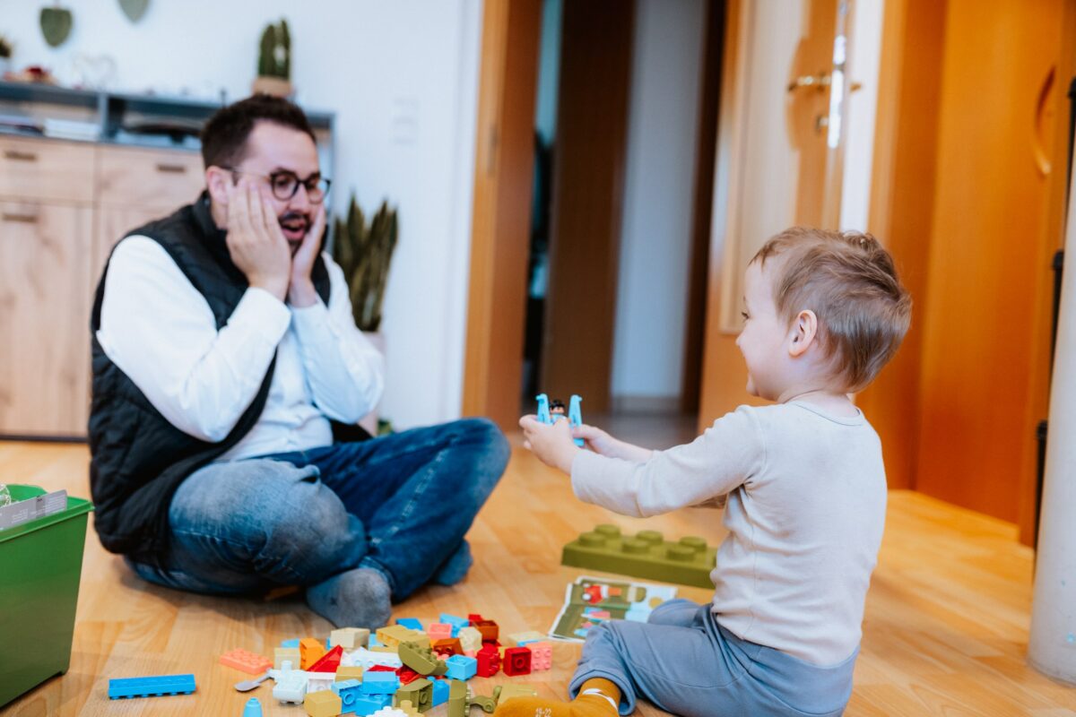 Marcel Resch spielt gemeinsam mit dem Kind am Boden mit Klemmbausteinen
